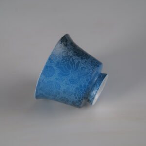 An inverted view of the Pale Ink Pool blue porcelain horseshoe cup highlighting its foot rim and detailed floral body engraving