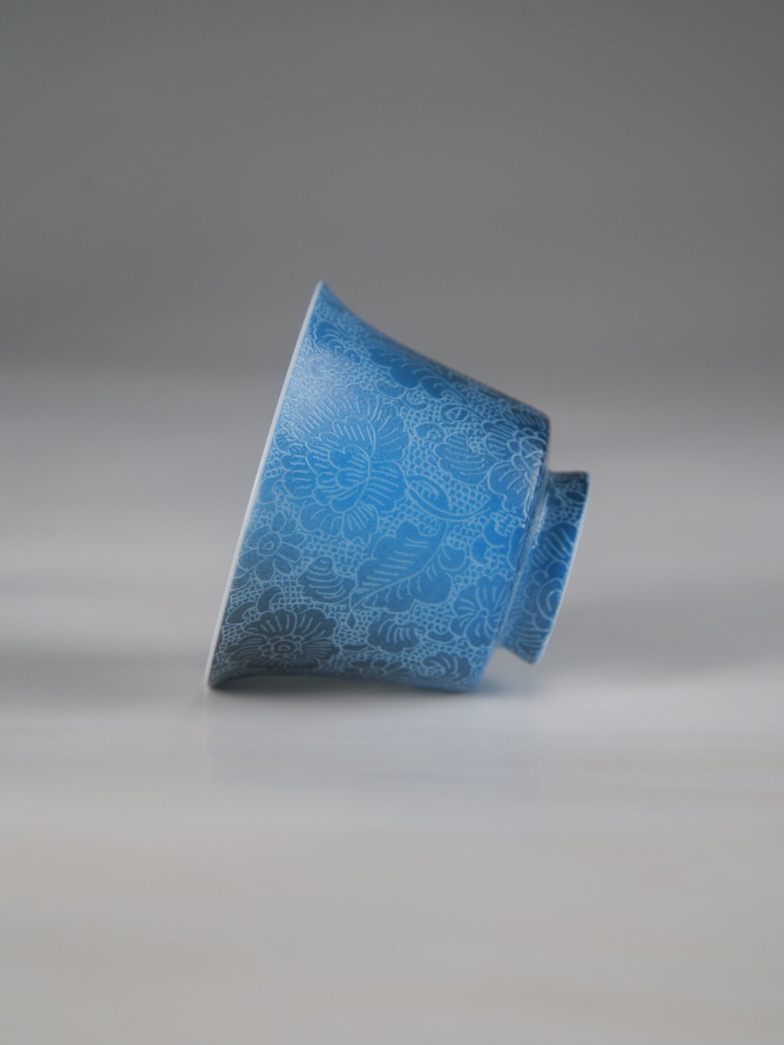 pale-ink-pool-blue-horseshoe-porcelain-cup-side-profile Side profile view of the Pale Ink Pool blue porcelain horseshoe cup lying on its side, showcasing its elegant shape and intricate floral carving