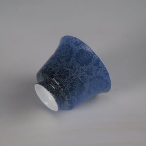 Tilted bottom perspective of the Pale Ink Pool blue porcelain horseshoe cup highlighting its foot rim and detailed floral body carving