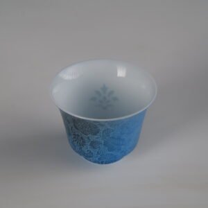 Top-down perspective of the Pale Ink Pool blue porcelain horseshoe cup showing the interior subtle watermark and rich outer floral engraving