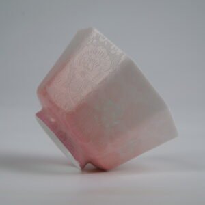 Tilted side view of the Peach Pink Gradient Octagonal Glazed Linglong porcelain cup lying on its side, showcasing its geometric octagonal shape, soft peach pink-to-white gradient glaze, and intricate carved floral patterns
