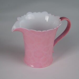 Tilted view of peach pink fair pitcher showing carved hundred flowers pattern and base