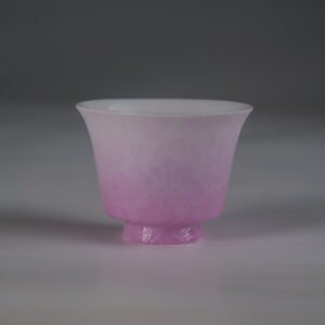 Front view of a pink gradient porcelain teacup with delicate embossed floral patterns, standing against a plain gray studio background.