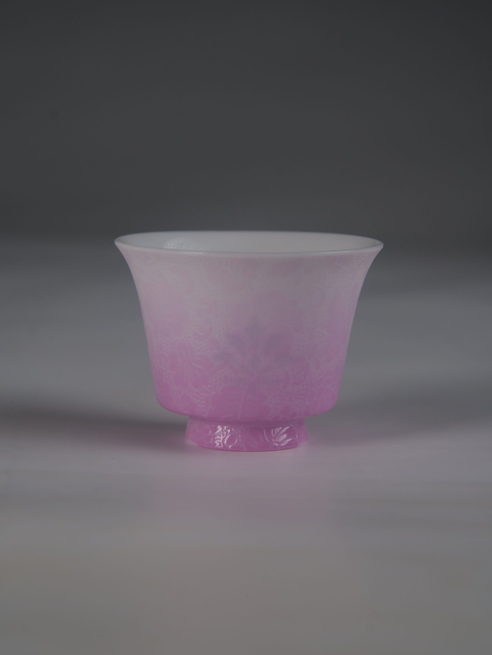pink-gradient-porcelain-teacup-front-view Front view of a pink gradient porcelain teacup with delicate embossed floral patterns, standing against a plain gray studio background.