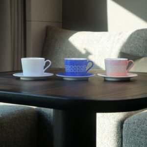 Eye level view of three porcelain coffee cup and saucer sets on dark wooden table in ambient light