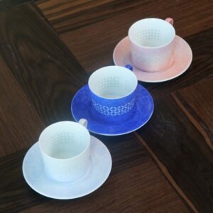 High angle view of porcelain coffee cups with saucers in white ultramarine blue and pink on dark wooden table