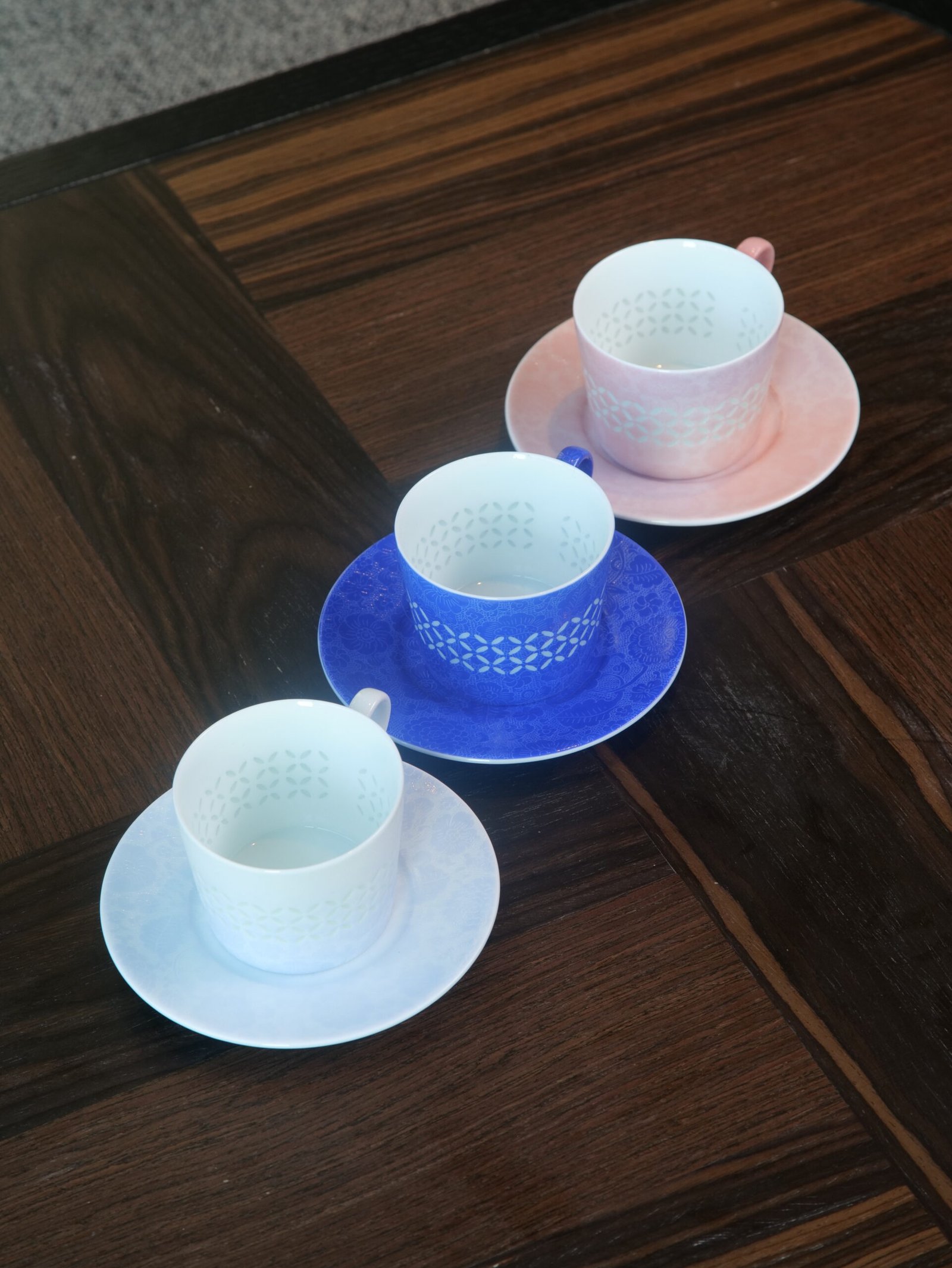 Porcelain Coffee Cup Saucer Sets – Trio High Angle View High angle view of porcelain coffee cups with saucers in white ultramarine blue and pink on dark wooden table