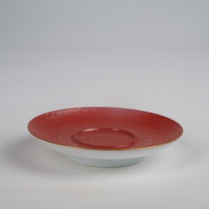 The red porcelain saucer of the Palace Red Elegant Charm Gaiwan set with a gold-gilded rim and embossed pattern on a plain white background.