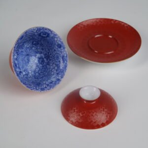 The complete 3-piece Palace Red Elegant Charm Gaiwan set laid out separately, fully displaying the blue floral interior of the cup, the textured red lid, and the matching saucer.