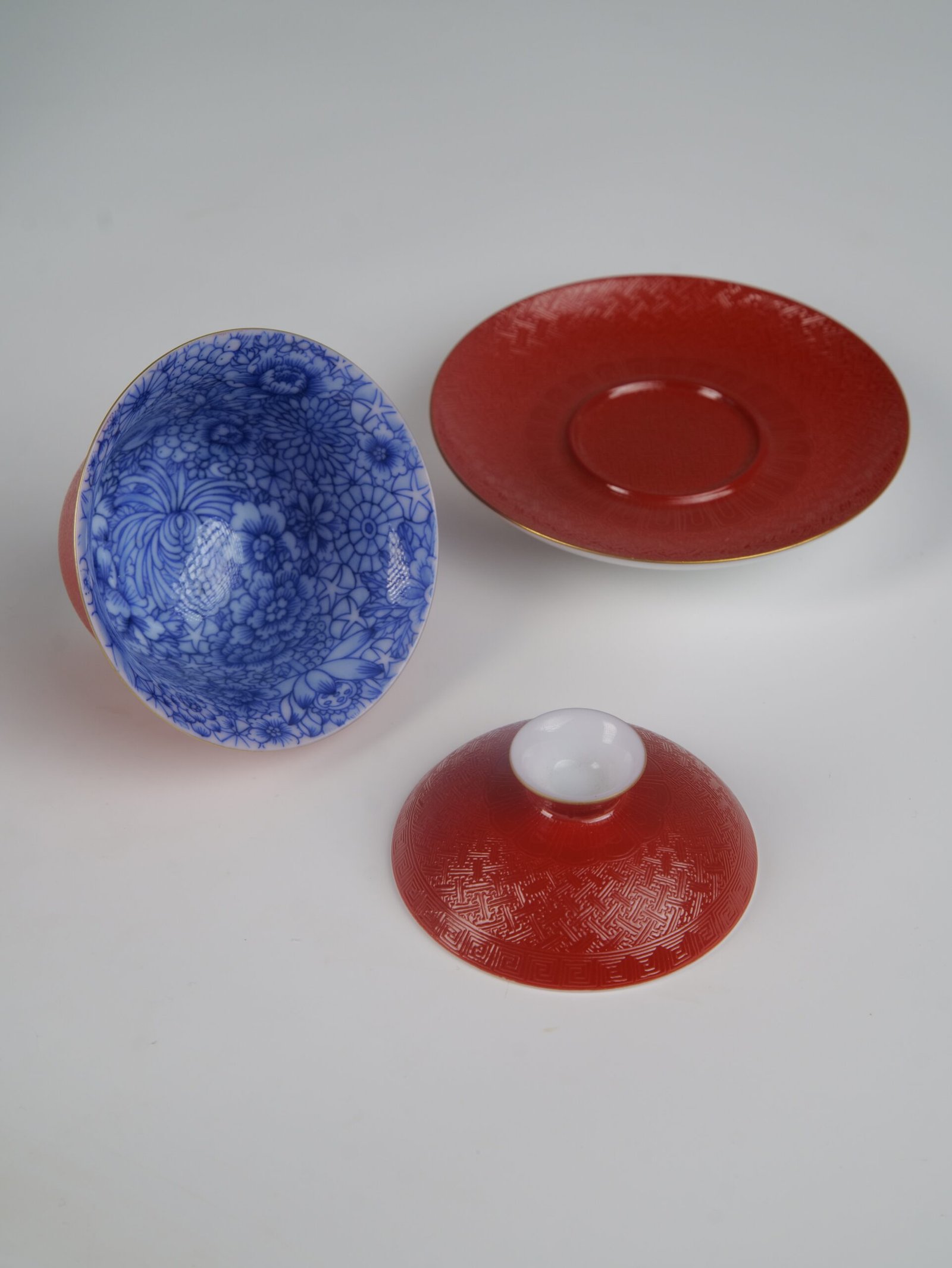 palace-red-elegant-charm-gaiwan-3-piece-set-laydown The complete 3-piece Palace Red Elegant Charm Gaiwan set laid out separately, fully displaying the blue floral interior of the cup, the textured red lid, and the matching saucer.