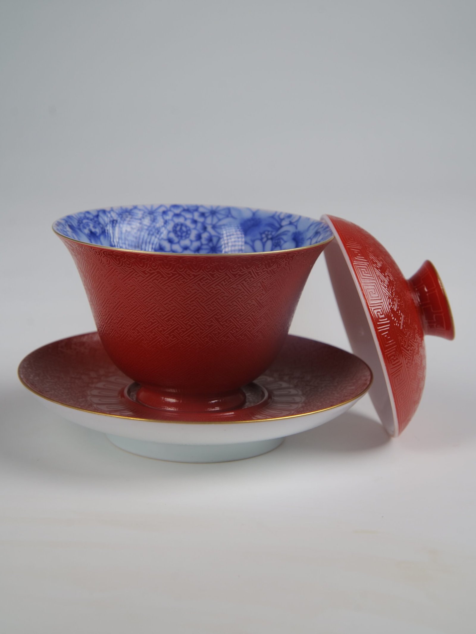 palace-red-elegant-charm-gaiwan-open-lid-blue-interior The Palace Red Elegant Charm Gaiwan with the lid removed, revealing the vibrant blue and white floral pattern lining the inside of the textured red cup, with the lid leaning against the saucer.