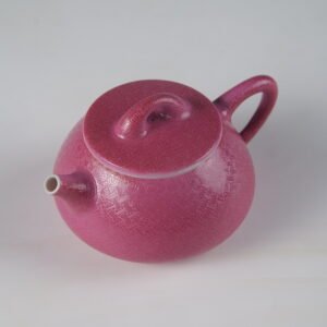Angled top view showing the spout and lid of a rouge red porcelain Shi Piao teapot on white background