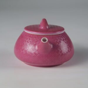 Front view facing the spout of a rouge red porcelain Shi Piao teapot with hand-carved Pa Hua details