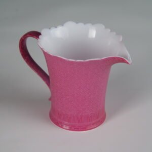 45-degree angle view of rouge red flower-rim fair pitcher with hand-carved swastika pattern showing spout and handle