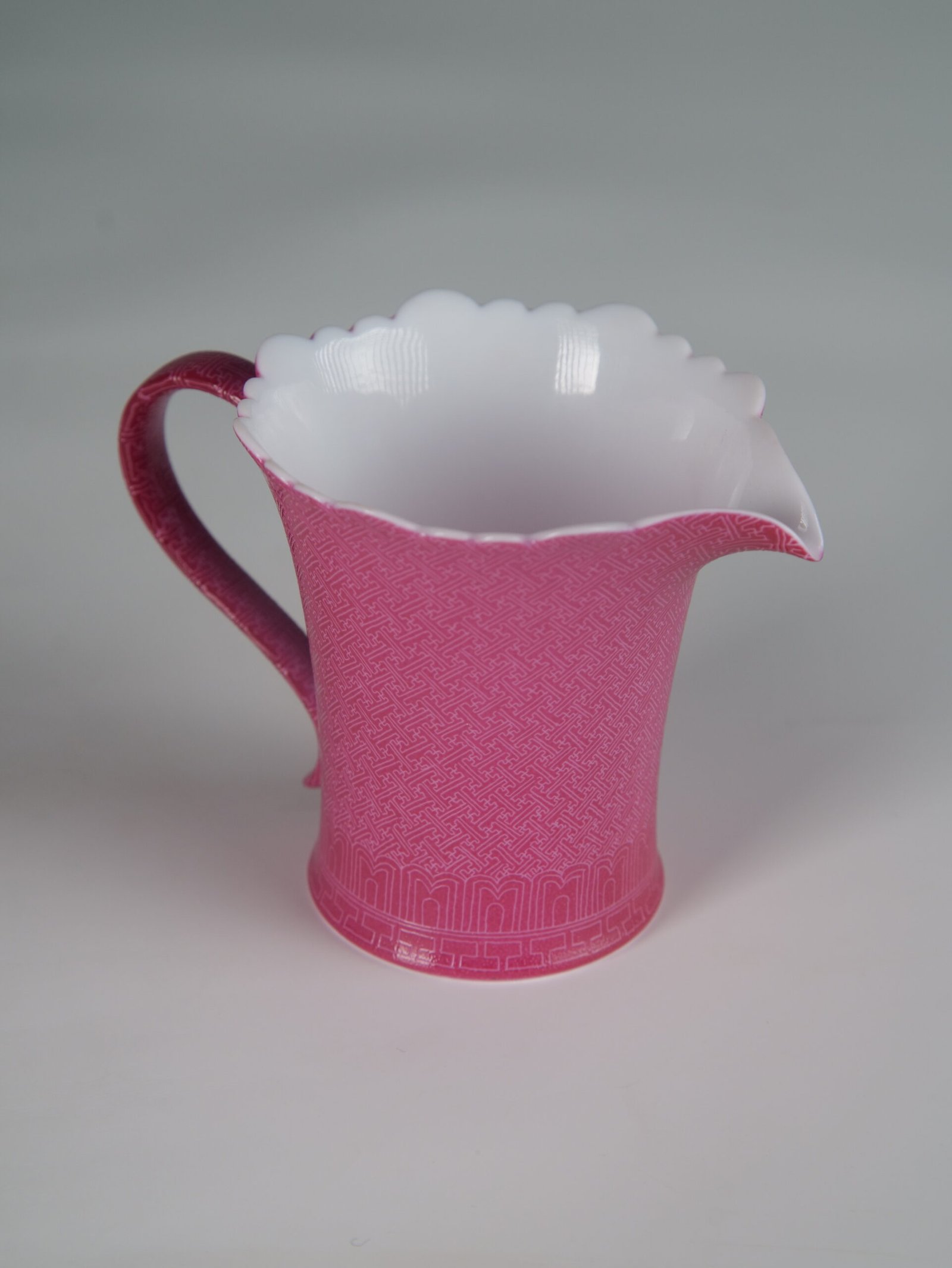 Rouge Red Swastika Pattern Fair Pitcher – Right Side Angle View 45-degree angle view of rouge red flower-rim fair pitcher with hand-carved swastika pattern showing spout and handle