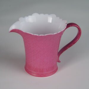 Tilted view of rouge red porcelain flower-rim fair pitcher showcasing hand-carved swastika Pa Hua pattern and white base