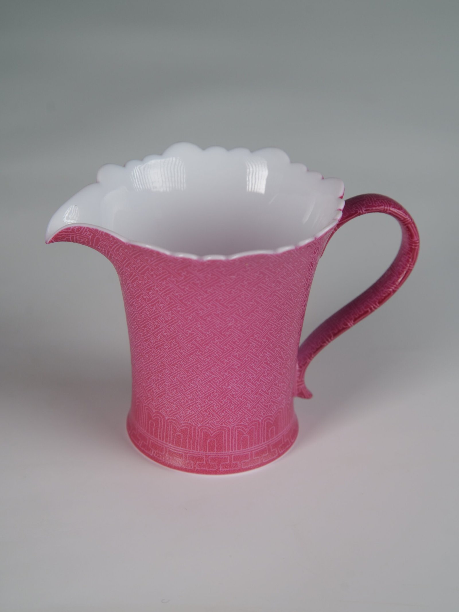 Rouge Red Swastika Pattern Fair Pitcher – Bottom and Texture Detail Tilted view of rouge red porcelain flower-rim fair pitcher showcasing hand-carved swastika Pa Hua pattern and white base