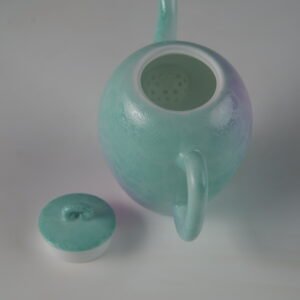 Top-down view of open spring glow gradient beauty shoulder teapot showing interior filter holes and lid on white background
