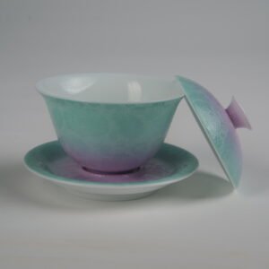 Side view of the complete Spring Glow Gradient Elegant Charm Gaiwan set with the lid resting against the cup, showing the white porcelain interior, soft pink and fresh green gradient glaze, and handcrafted Pa Hua floral pattern