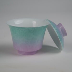 Side view of the Spring Glow Gradient Horseshoe Gaiwan without saucer, showing its lid resting against the open cup, white porcelain interior, soft pink-purple and green gradient glaze, and fine engraved Pa Hua daylily patterns