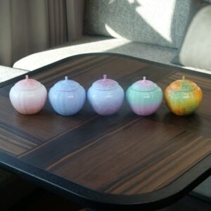 Five colorful gradient porcelain melon-shaped jars displayed on a dark wooden tea table