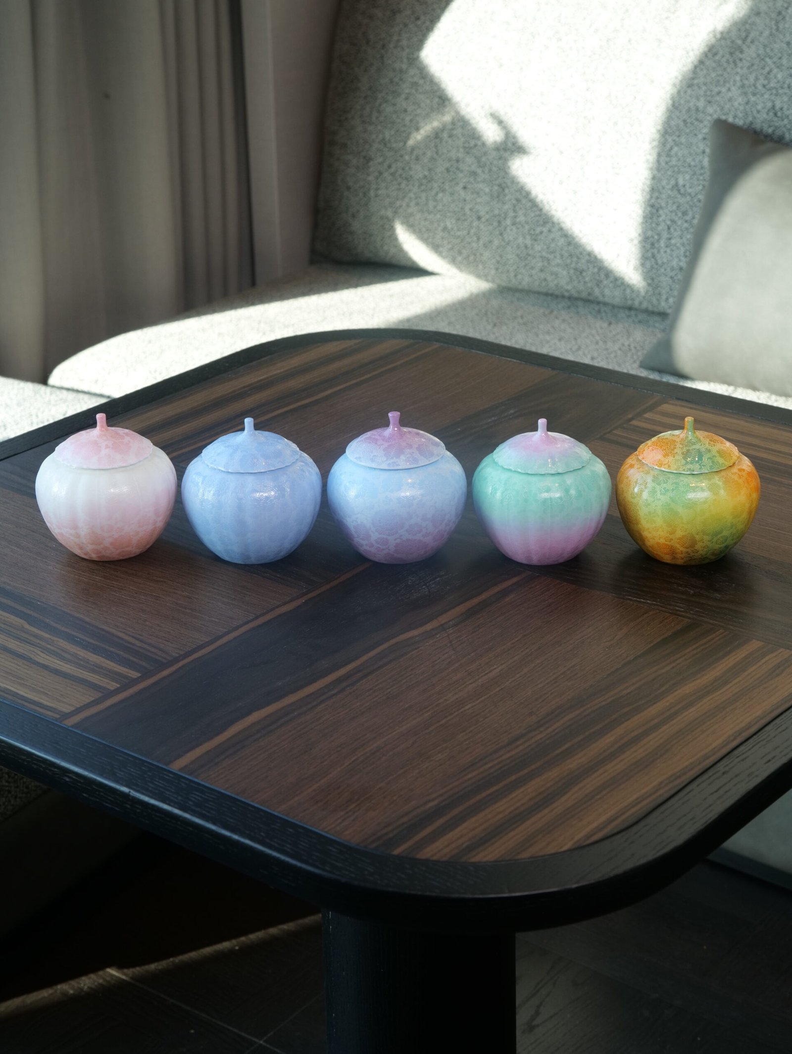 Spring Glow Gradient Melon Jars – Tea Table Display Five colorful gradient porcelain melon-shaped jars displayed on a dark wooden tea table
