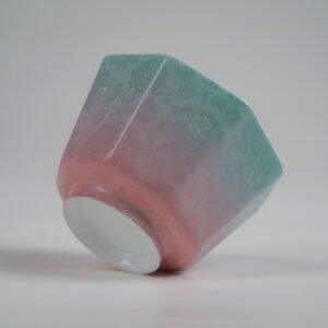 Side profile view of the Spring Glow Gradient Octagonal Glazed Linglong porcelain cup lying on its side, showing its geometric shape, base, and detailed green-to-pink gradient carved floral texture