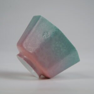 Tilted side view of the Spring Glow Gradient Octagonal Glazed Linglong porcelain cup lying on its side, featuring vibrant green-to-pink gradient tones and intricate carved floral patterns