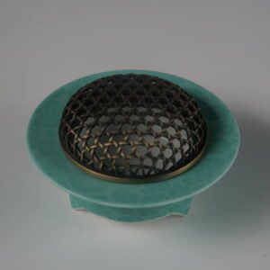 Angled view of turquoise ceramic incense burner with woven copper lid