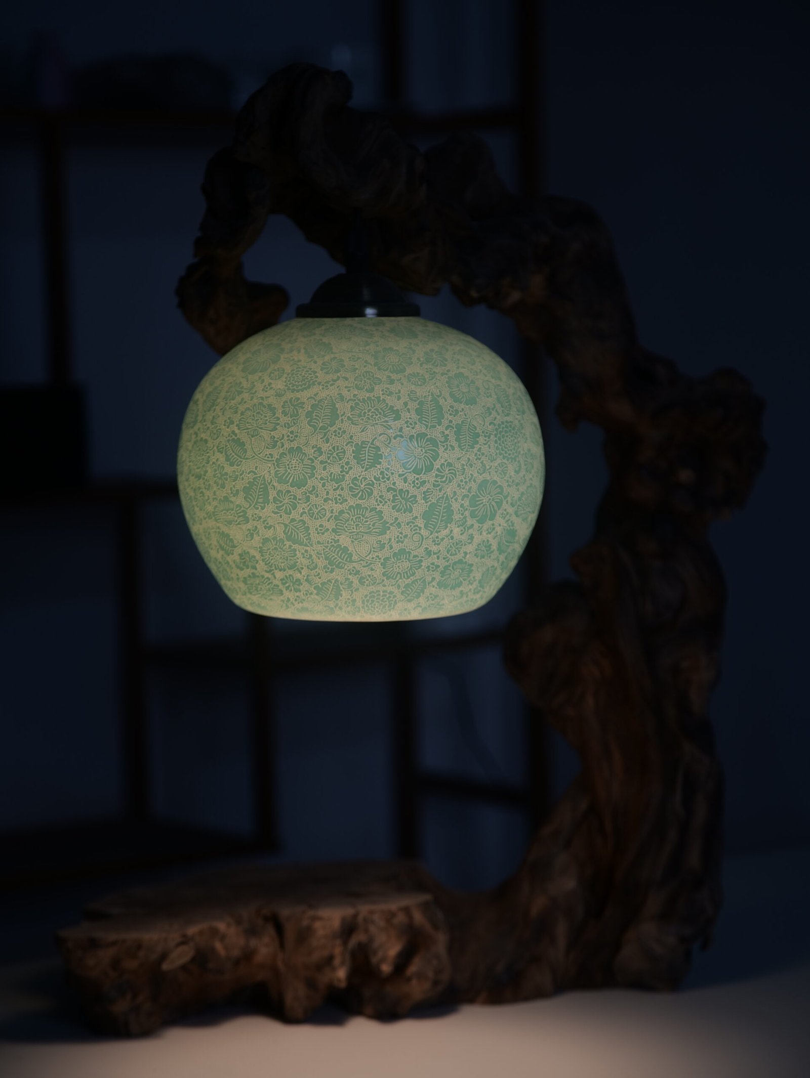 Treasure Jar Lampshade - Lifestyle View Lit turquoise green carved porcelain lampshade hanging on a rustic wooden stand