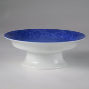 Side view of blue and white porcelain pedestal plate against white background
