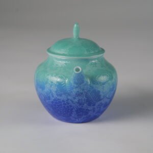 Eye-level front view facing the spout of a verdant blue Pan's porcelain teapot on white background