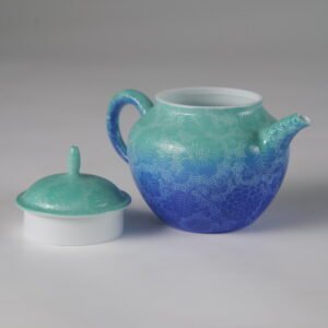 Side view of verdant blue porcelain Pan's teapot with lid off on white background