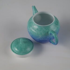 Top-down view of open verdant blue Pan's teapot showing interior filter holes and lid on white background