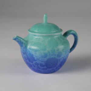 Side view of verdant blue Pan's teapot with hand-carved hundred flowers Pa Hua pattern on a plain white background