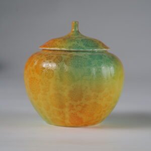 Eye level front view of verdant clouds with orange hues melon-shaped jar with hundred flowers pattern