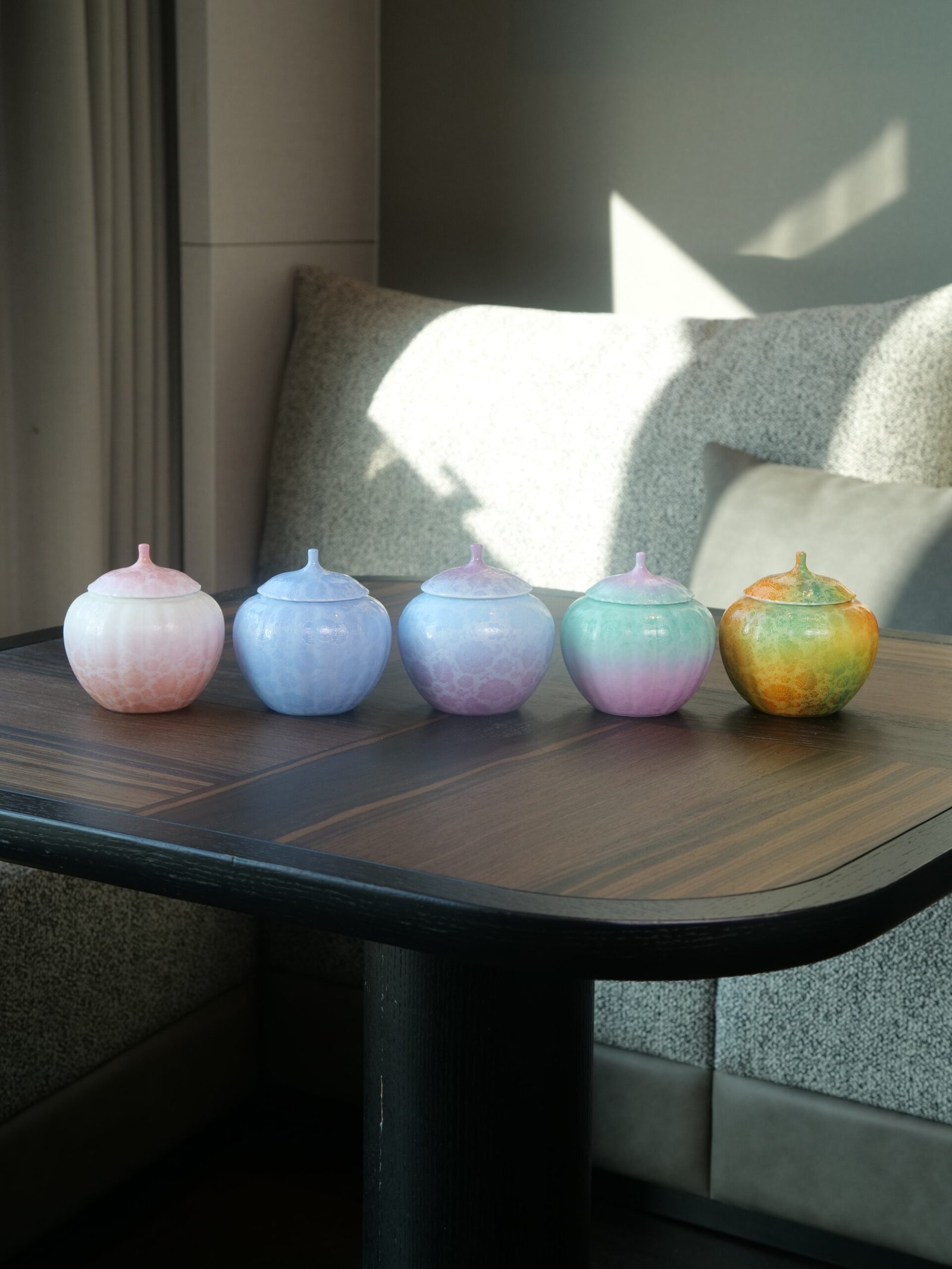 Verdant Clouds with Orange Hues Melon Jars – Tea Table Display Five colorful gradient porcelain melon-shaped jars arranged in a row on a wooden tea table