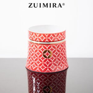 Red carved porcelain cup with gold accents reflected on a sleek black surface