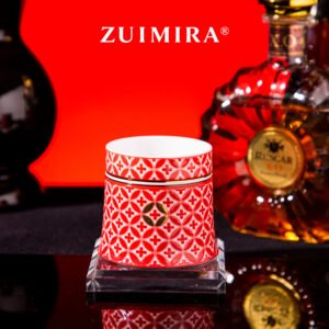Red rotatable ceramic cup displayed on a clear coaster next to a liquor bottle